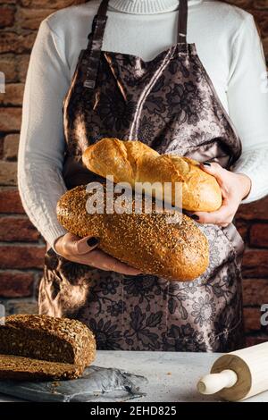 Faceless female artisan in apron with different types of bread with golden crust and sunflower seeds Stock Photo