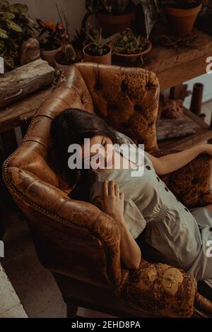 From above of peaceful female sitting in shabby leather chair while relaxing at home Stock Photo