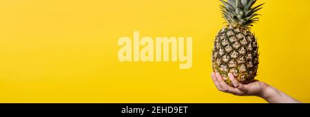 Hand of unknown woman holding pineapple - female hold fresh fruit on bright yellow background - healthy eating and diet modern concept Stock Photo