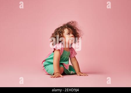 Adorable toddler child in dress with curly hair having a tantrum looking away leaning sitting on the on floor Stock Photo