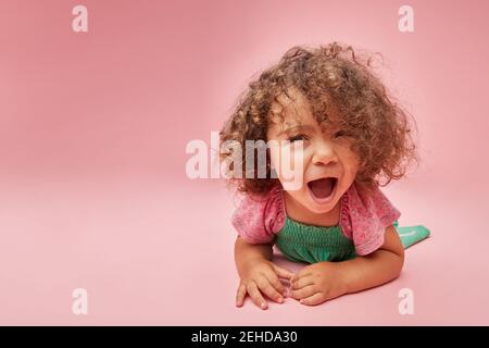 Adorable toddler child in dress with curly hair having a tantrum looking away leaning sitting on the on floor Stock Photo