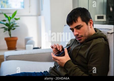 Male with eyesight disability scrolling mobile phone while sitting on couch at home Stock Photo