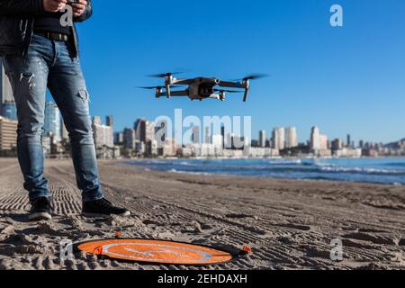 From above of cropped unrecognizable male with remote controller standing on beach with drone placed on landing pad Stock Photo