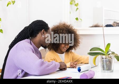 Smiling African American dad sitting at table with girl surfing netbook while preparing task for school Stock Photo