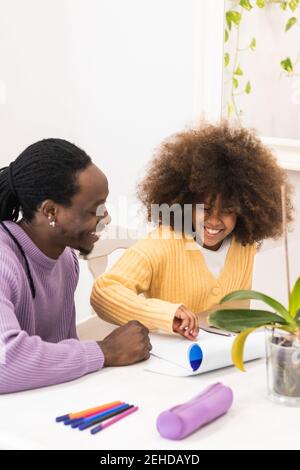 Smiling African American dad sitting at table with girl surfing netbook while preparing task for school Stock Photo