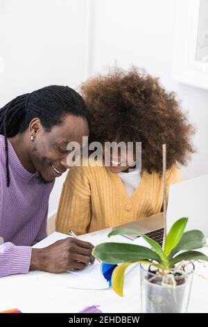 Smiling African American dad sitting at table with girl surfing netbook while preparing task for school Stock Photo