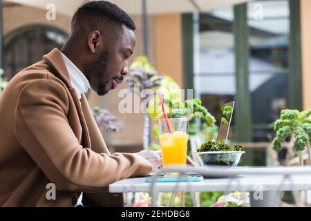 Young African American businessman browsing on laptop while looking down at cafeteria table Stock Photo