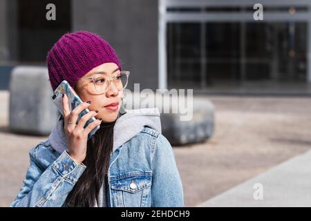 Portrait of an Asian Woman with a purple hat on the street with a cellphone in hand Stock Photo