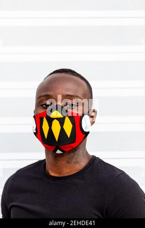 Young African American male looking at camera in bright mask with ornament during coronavirus period on light background Stock Photo