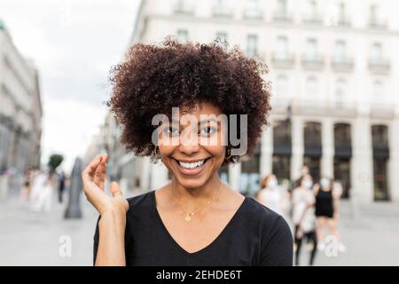 Young cheerful African American female with Afro hairstyle looking at camera on city street Stock Photo
