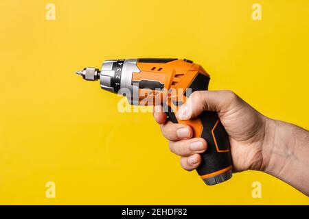 Hand of unknown man holding electric screwdriver - male hold work craft tool on bright yellow background - repair renovation electric equipment tools