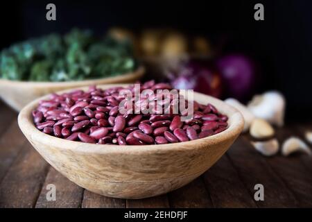 Wooden bowl full of dried red beans with kale, garlic and other ingredinets in the background Stock Photo