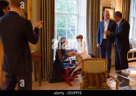 President Barack Obama talks with the Duke of Cambridge while the Duchess of Cambridge plays with Prince George; at left First Lady Michelle Obama talks with Prince Henry of Wales, at Kensington Palace in London April 22, 2016. Stock Photo