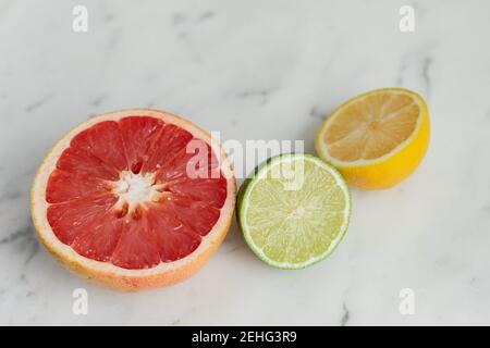 Fresh citrus grapefruit, lemon, and lime, cut on a marble backdrop Stock Photo