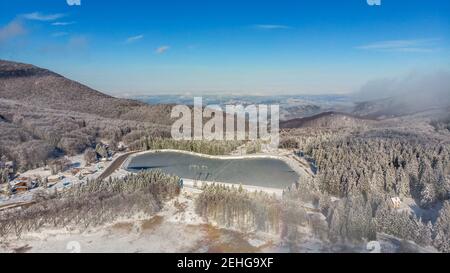 Flying above snowy winter misty mountain forest covered with snow . Top view, landscape with drifting fog through the trees in the morning. Stock Photo