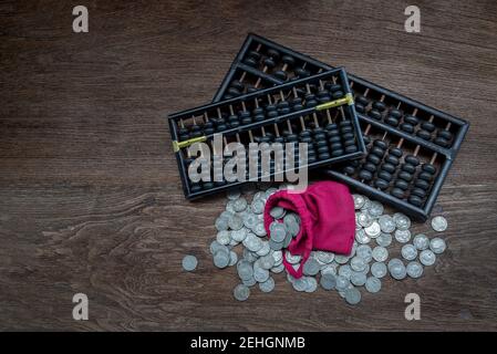 Vintage wooden hand abacus with pile of money coins from red cloth bag on rustic old wooden table. Concept for making business and saving money of chi Stock Photo