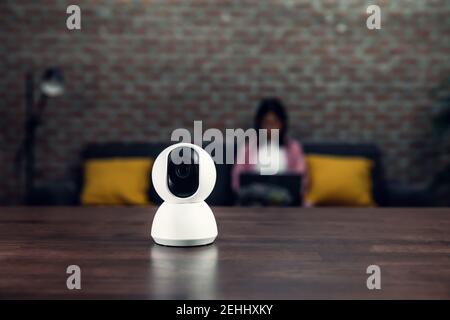 Security CCTV camera, surveillance technology on the table and blur background woman sitting on sofa. Stock Photo