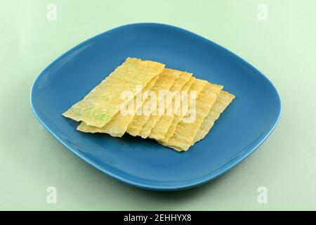 Wasabi potato chip strips on blue snack plate on light green background Stock Photo
