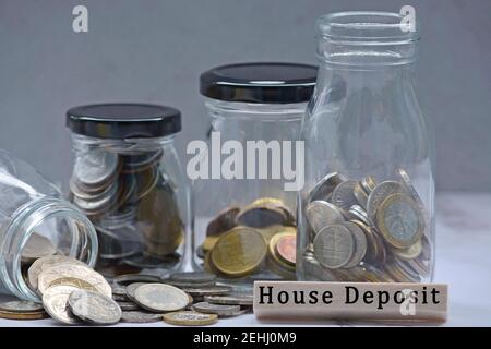 Text on wood block and glass jars with multicurrency coins and blurred background - House deposit Stock Photo