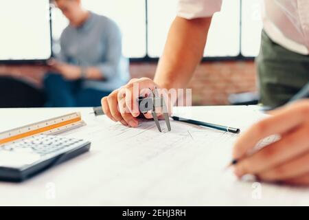 Engineering hands hold vernier caliper working and checking drawing blue print scale on workplace. Stock Photo