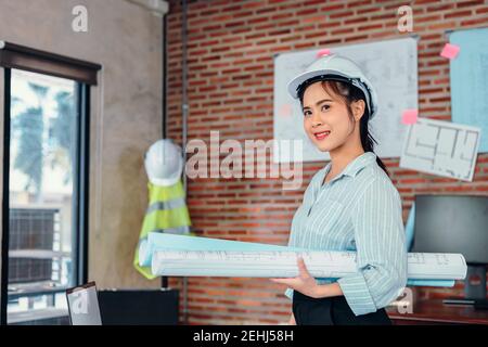 Portrait Asian engineer woman hold engineer drawing design blue print at room site construction. Stock Photo