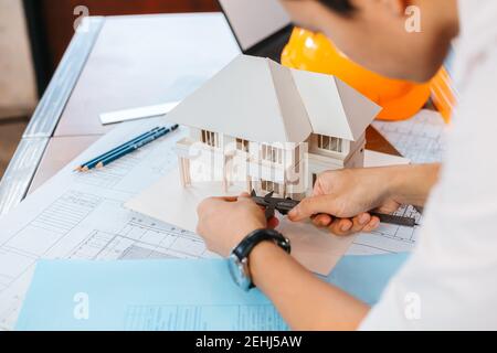Engineering hands hold vernier caliper working and checking house model scale between meeting with businessman and businesswoman. Stock Photo