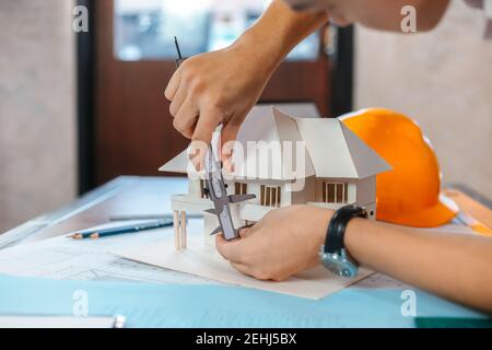 Engineering hands hold vernier caliper working and checking house model scale between meeting with businessman and businesswoman. Stock Photo