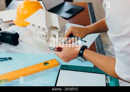 Engineering hands hold vernier caliper and pen for working and checking drawing paper plan and house model. Stock Photo