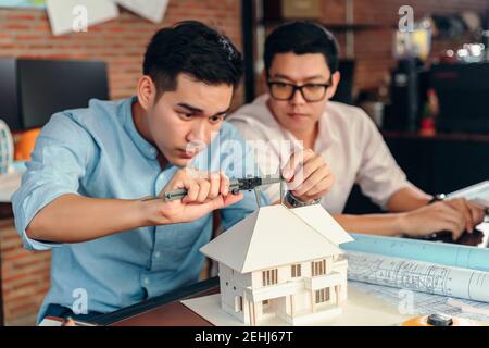 Engineering hands hold vernier caliper working and checking house model scale between meeting with businessman and businesswoman. Stock Photo