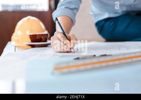 engineers holding a pen pointing to a building and  drawing outlay construction plan as guide for builders with details. Engineer design and writing b