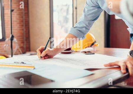 engineers holding a pen pointing to a building and  drawing outlay construction plan as guide for builders with details Stock Photo