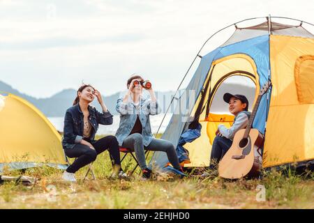 A group of friends camping near the lake. Women use binoculars to look at birds in the sky. Stock Photo
