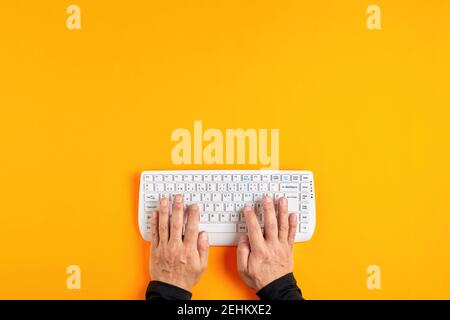 Male hands using a white computer keyboard on yellow background. Stock Photo