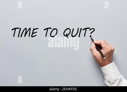 Businessman hand writing the question of time to quit on gray background. Deciding to quit job or to exit business concept. Stock Photo