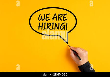 Male hand drawing a speech balloon with the message of we are hiring on yellow background. Job employment or job advert concept. Stock Photo