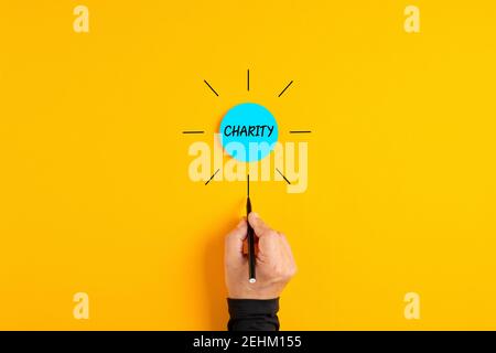 The word charity written on a blue circle badge with male hand drawing rays around it. Stock Photo