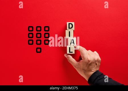 Male hand arranging the wooden blocks with the word dial on red background. Customer assistance, help service or emergency call concept. Stock Photo