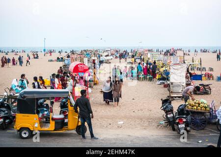 Visitors to Chennai Marina beach to enjoy the cool evening sea breeze with shops on either side of walkway Stock Photo