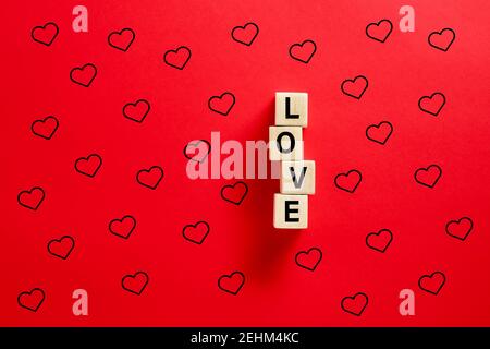 The word love on wooden blocks with heart shapes on red background. Love and valentines day concept. Stock Photo