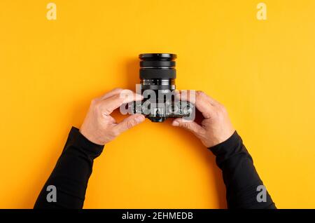 Male hands hold digital photo camera against yellow background with copy space. Overhead top view. Stock Photo