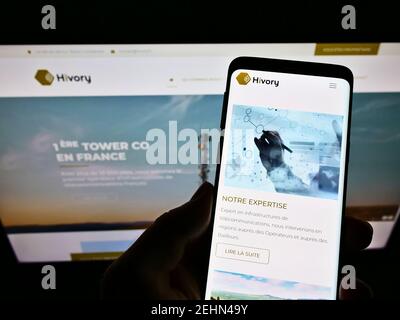 Person holding mobile phone with website and logo of French telecoms tower company Hivory in front of screen. Focus on top-left of phone display. Stock Photo