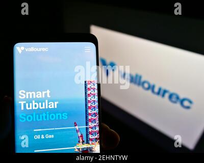 Person holding smartphone with website of French steel tube manufacturer Vallourec SA on screen in front of logo. Focus on center of phone display. Stock Photo