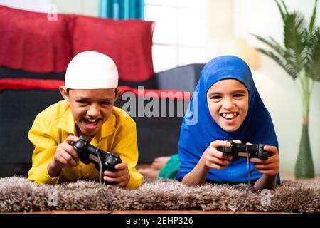 Two muslim sibling kids playing videogame using joystick while lying on floor at home - Concept of children unhealthy playing position and gaming Stock Photo