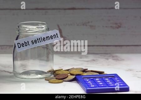 Glass jars with blurred multicurrency coins, calculator and text on white torn paper - Debt settlement Stock Photo