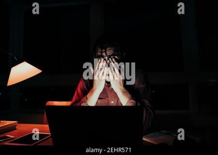 Stressed caucasian male freelancer working late at night finishing assignments sitting at laptop in home office Stock Photo