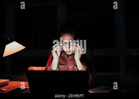 Stressed caucasian male freelancer adjusting spectacles working late at night on laptop  Stock Photo
