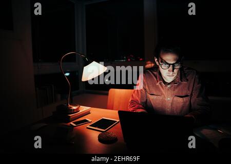 Caucasian male freelancer working sorting emails on laptop working late at night Stock Photo