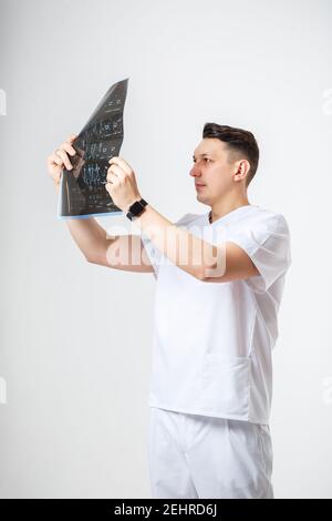 Young male doctor in white surgical suit holding and examining an MRI scan of the patient's head .Isolated on white background Stock Photo
