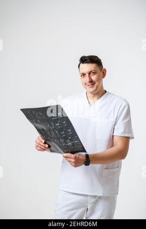 Young male doctor in white surgical suit holding and examining an MRI scan of the patient's head .Isolated on white background Stock Photo