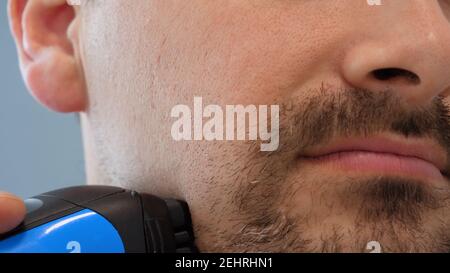 Male hand shaves stubble with electric razor Stock Photo
